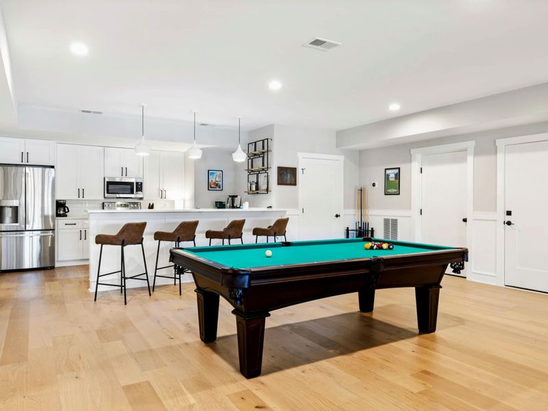A spacious entertainment area featuring a pool table, a modern kitchenette with bar seating, and ample space for relaxation and fun.