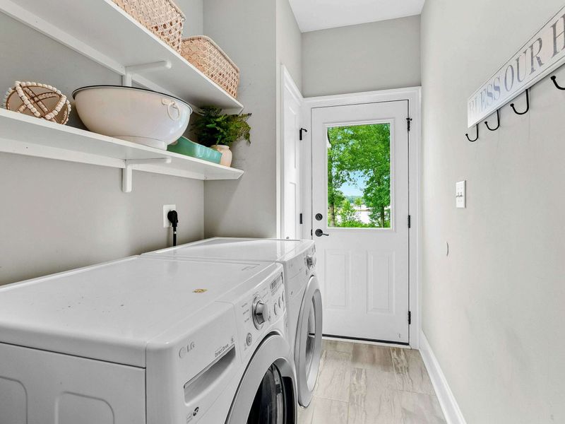 A bright and functional laundry room featuring modern appliances, open shelving for storage, and convenient access to the outdoors.