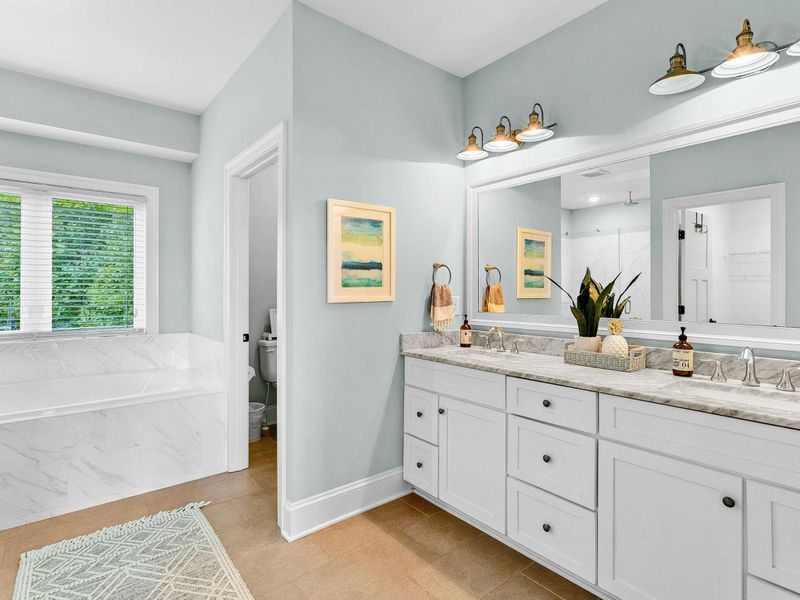 A luxurious ensuite bathroom featuring a double vanity with ample storage, a glass-enclosed rainfall shower, a soaking tub, and elegant marble finishes.