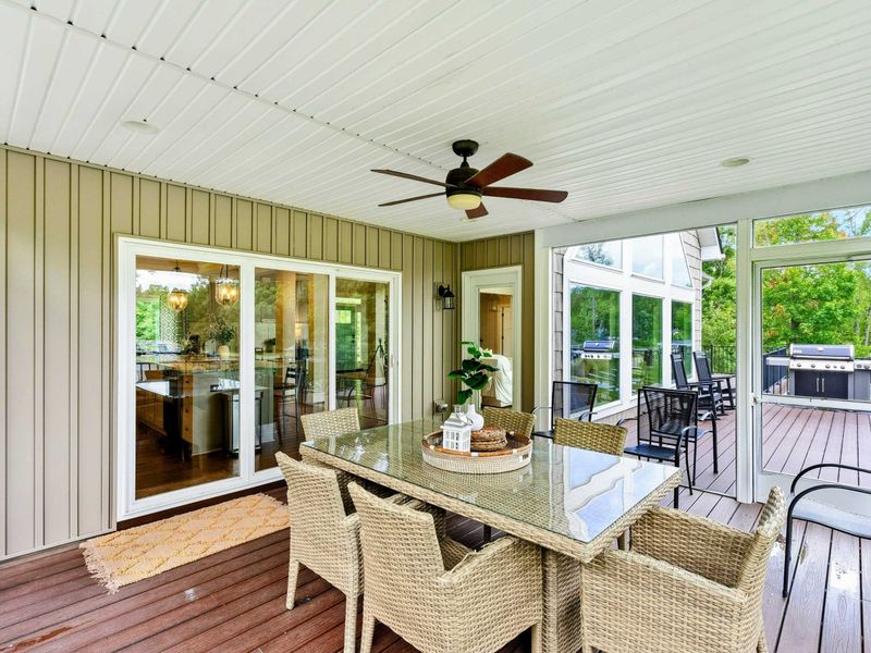 A cozy screened-in porch with a dining area, ceiling fan, and stunning lake views, seamlessly connected to the outdoor deck and main living space.