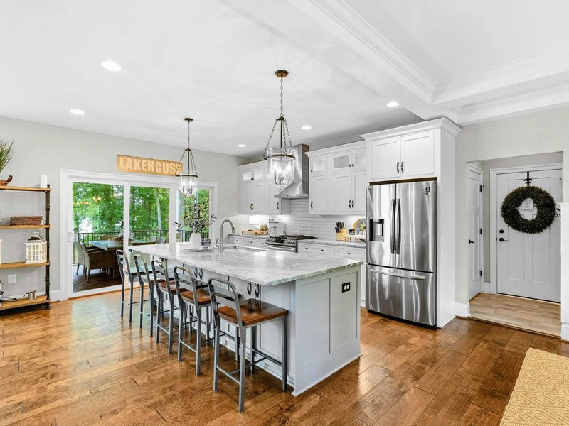 A spacious and modern kitchen with a large marble island, high-end appliances, elegant pendant lighting, and open access to the dining and living areas with views of the backyard.