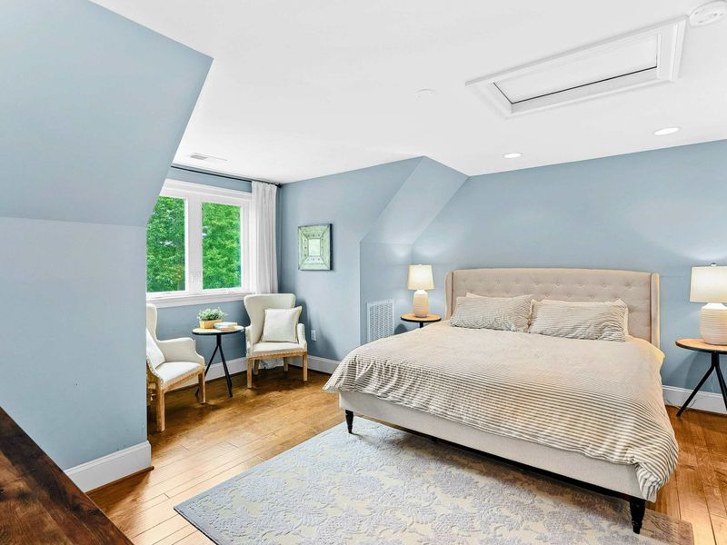 A serene bedroom with a king bed, soft blue walls, a cozy seating area by the window, and an ensuite bathroom for added privacy.