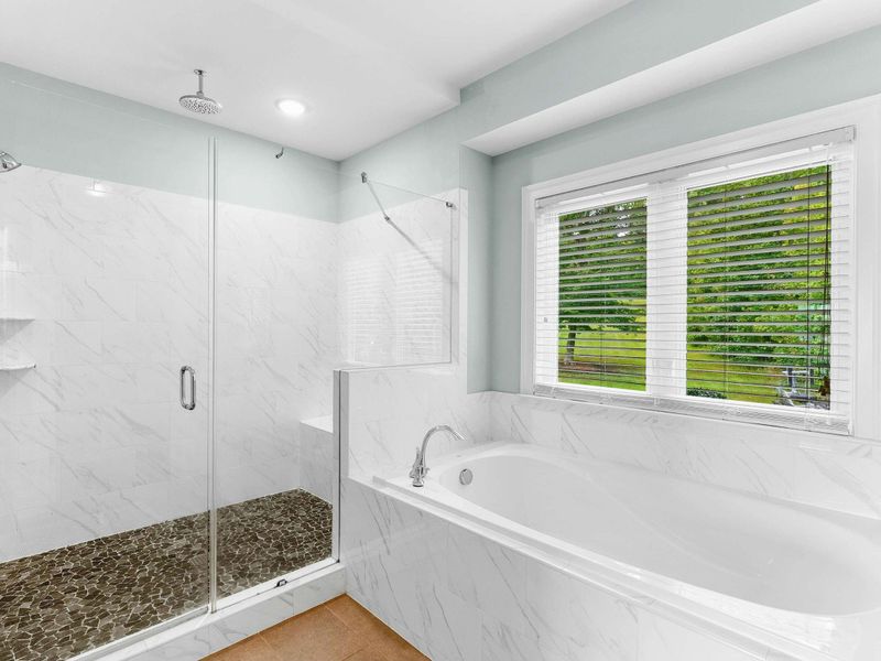 A luxurious ensuite bathroom featuring a double vanity with ample storage, a glass-enclosed rainfall shower, a soaking tub, and elegant marble finishes.