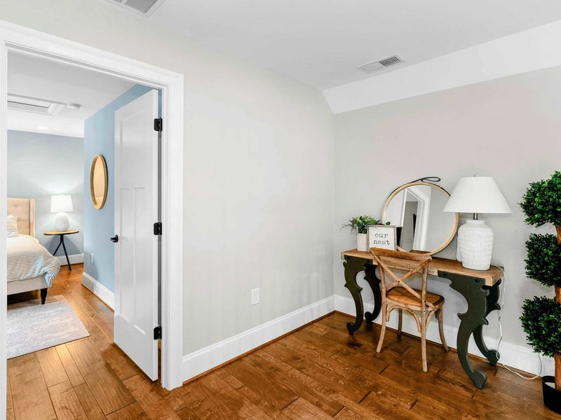 An open and airy loft space featuring a stunning view of the living room and large windows, a cozy workspace with elegant decor, and a hallway leading to private bedrooms.