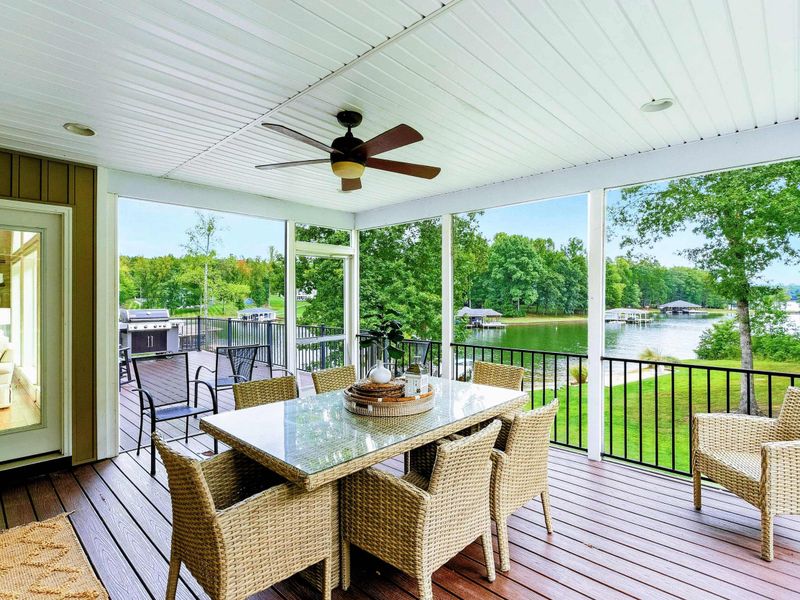 A cozy screened-in porch with a dining area, ceiling fan, and stunning lake views, seamlessly connected to the outdoor deck and main living space.