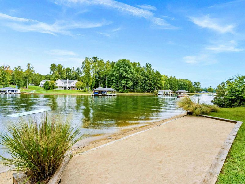 A private sandy beach area with a peaceful view of the lake, surrounded by lush greenery and nearby boat docks.