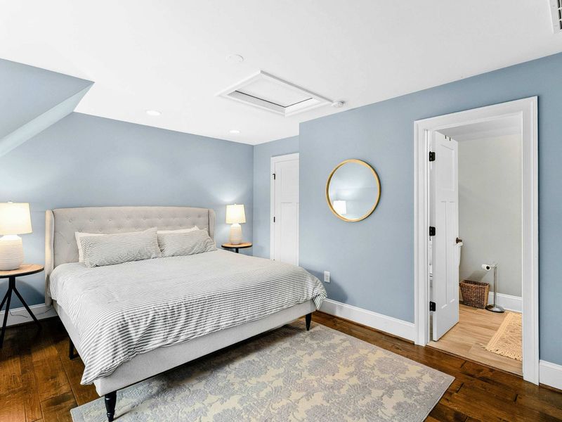 A serene bedroom with a king bed, soft blue walls, a cozy seating area by the window, and an ensuite bathroom for added privacy.
