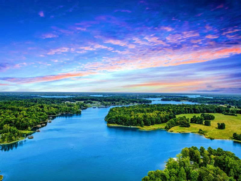 A breathtaking aerial view of Lake Anna showcasing its serene blue waters, lush green shoreline, and a vibrant, colorful sunset.
