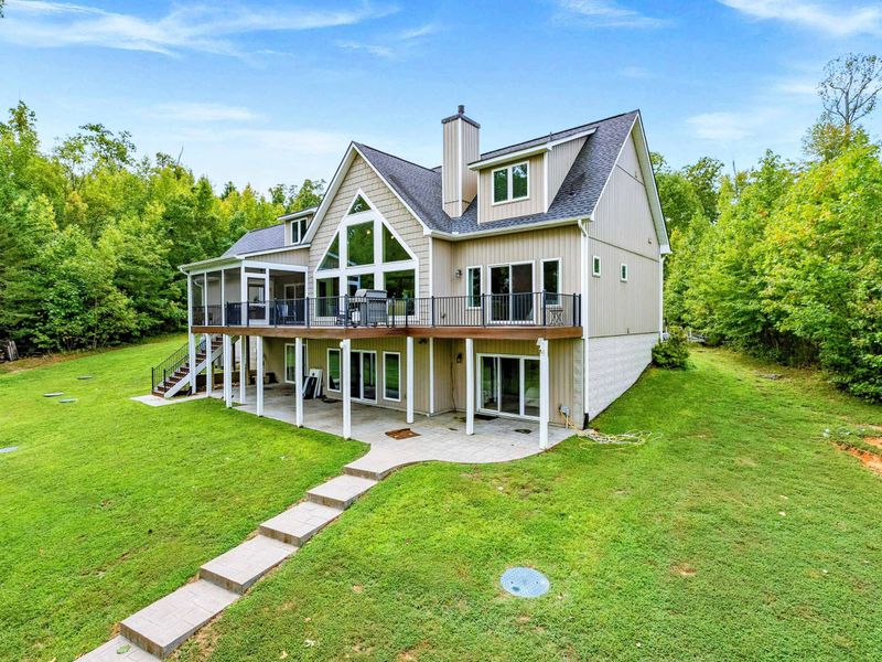 A stunning multi-level lake house with expansive windows, outdoor decks, and a spacious backyard surrounded by lush greenery.