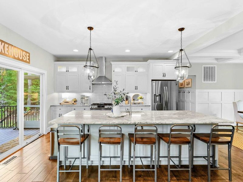 A spacious and modern kitchen with a large marble island, high-end appliances, elegant pendant lighting, and open access to the dining and living areas with views of the backyard.