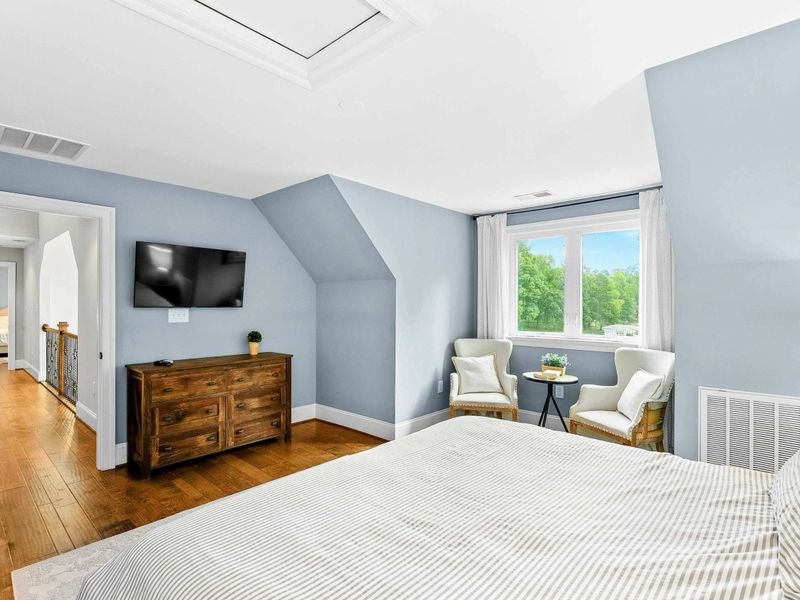 A serene bedroom with a king bed, soft blue walls, a cozy seating area by the window, and an ensuite bathroom for added privacy.