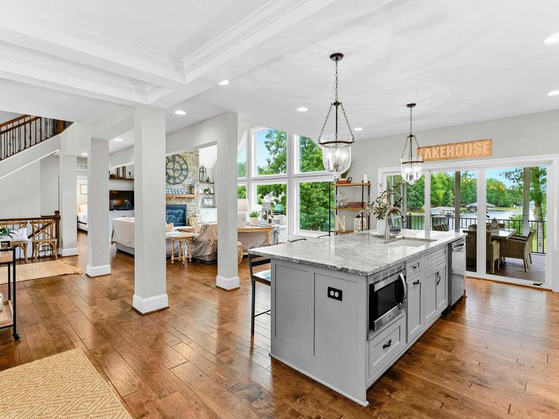 A spacious and modern kitchen with a large marble island, high-end appliances, elegant pendant lighting, and open access to the dining and living areas with views of the backyard.