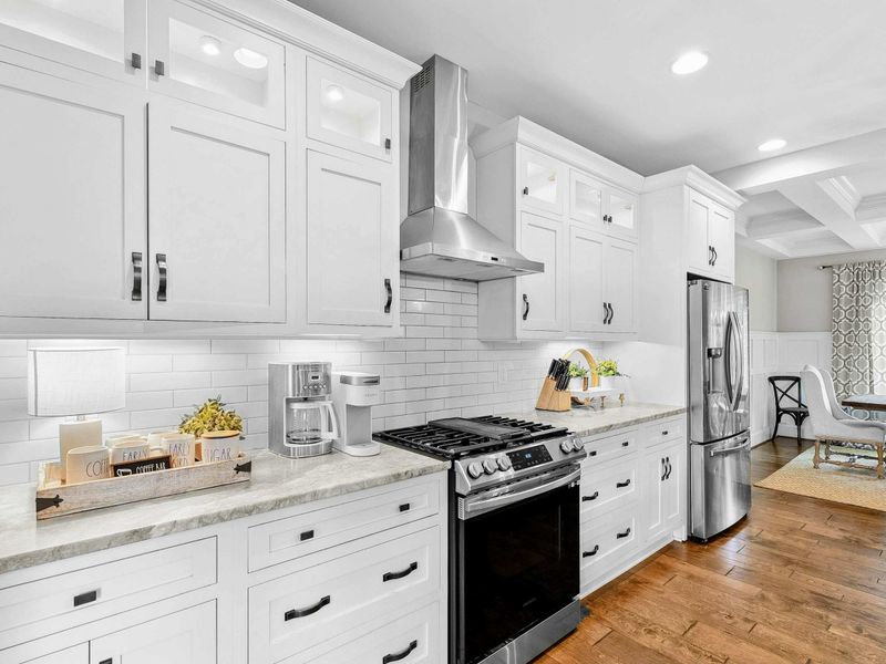 A spacious and modern kitchen with a large marble island, high-end appliances, elegant pendant lighting, and open access to the dining and living areas with views of the backyard.