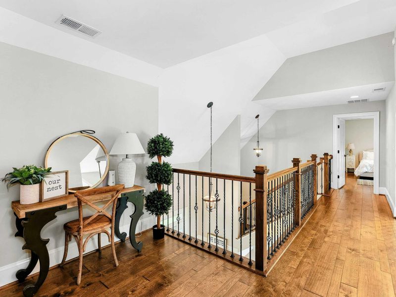 An open and airy loft space featuring a stunning view of the living room and large windows, a cozy workspace with elegant decor, and a hallway leading to private bedrooms.