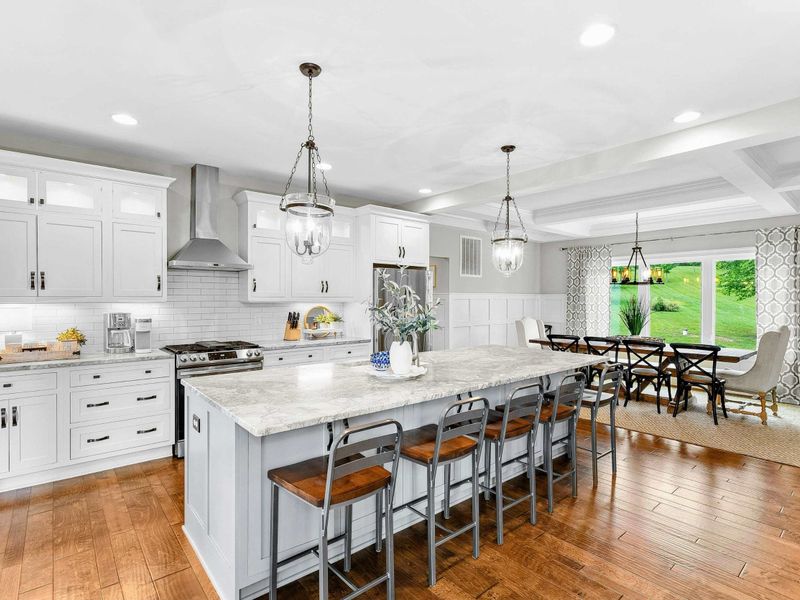 A spacious and modern kitchen with a large marble island, high-end appliances, elegant pendant lighting, and open access to the dining and living areas with views of the backyard.