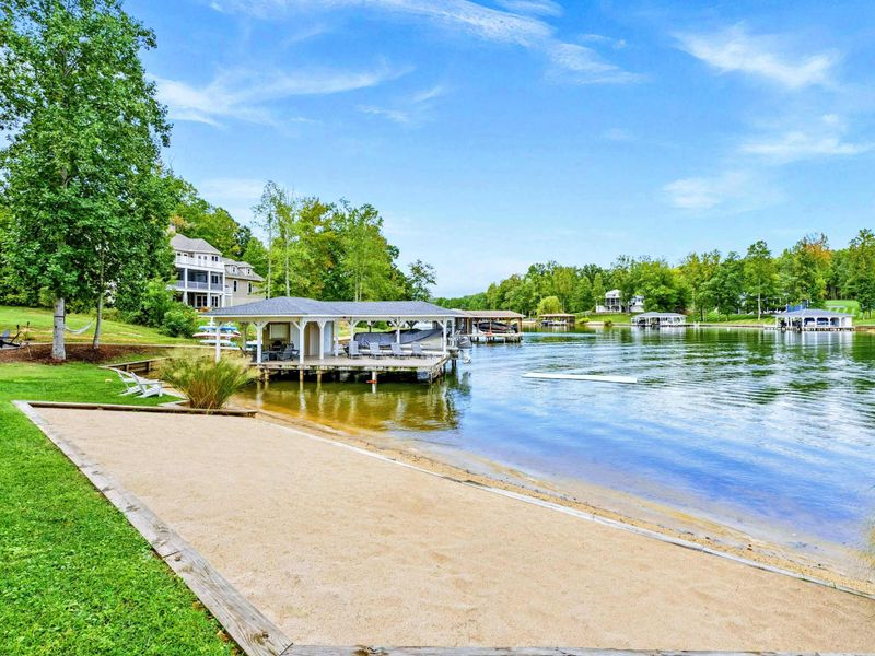 A private sandy beach area with a peaceful view of the lake, surrounded by lush greenery and nearby boat docks.