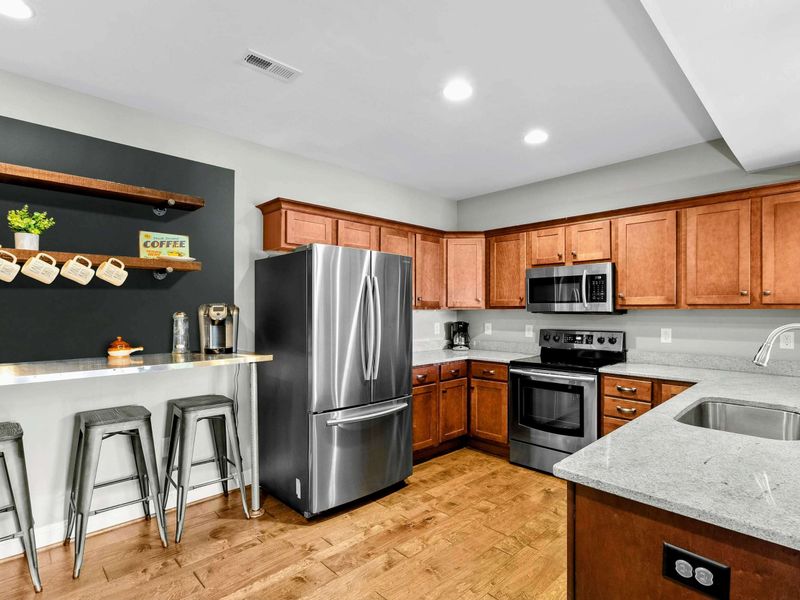A cozy lower-level kitchen with modern appliances, a rustic accent bar, seating areas, and direct access to the living space and backyard.