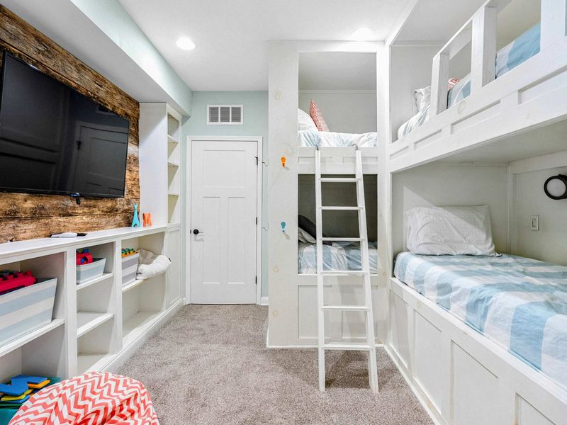 A fun and cozy bunk room featuring built-in beds, a large TV, ample storage for toys and games, and easy access to the main living areas.