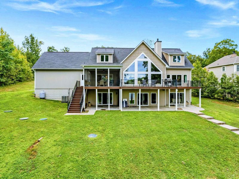 A stunning multi-level lake house with expansive windows, outdoor decks, and a spacious backyard surrounded by lush greenery.