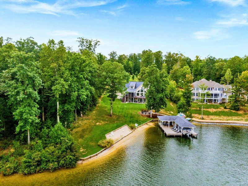 A picturesque lakeside property featuring a spacious home, private dock, sandy shoreline, and lush greenery for a tranquil retreat.