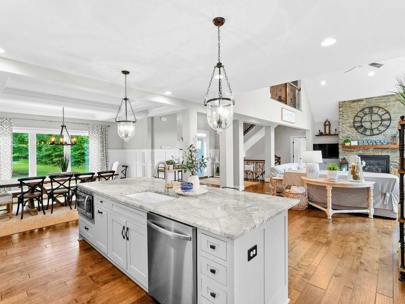 A spacious and modern kitchen with a large marble island, high-end appliances, elegant pendant lighting, and open access to the dining and living areas with views of the backyard.