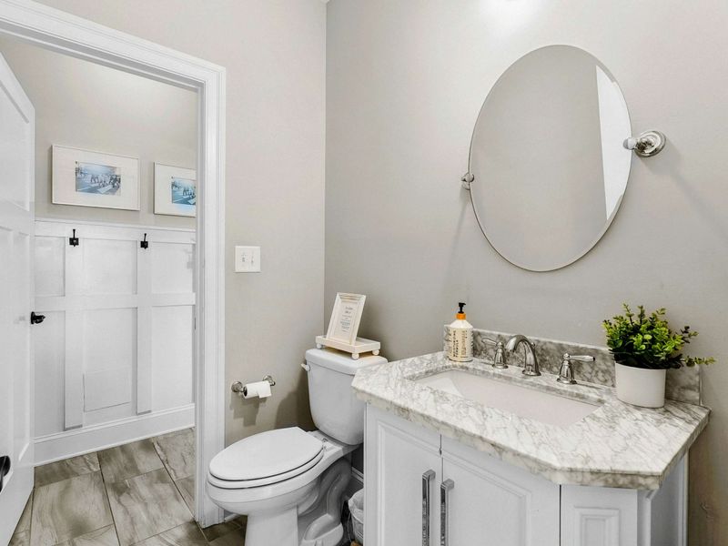 A stylish half-bath featuring a marble-topped vanity, a round mirror, and elegant decor for a welcoming touch.