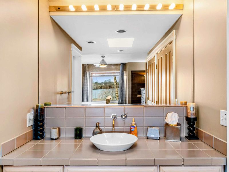 Primary Suite Ensuite with Lake Views - This elegant ensuite features a stylish vessel sink, ample counter space, and a large mirror with vanity lighting. Enjoy a relaxing retreat with beautiful lake views right from your bathroom.