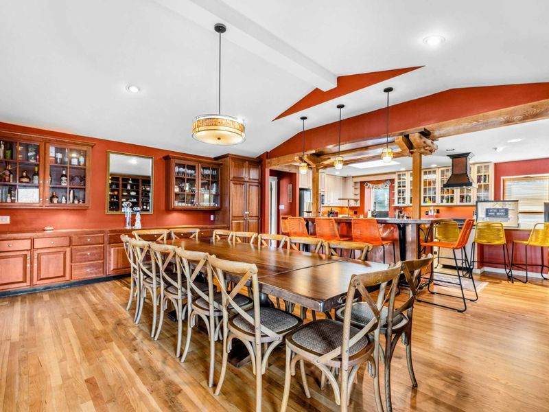 Spacious Dining & Entertaining Area - Enjoy meals at the large dining table with seating for twelve, seamlessly connected to the open kitchen and bar area. Perfect for gatherings, with warm wood tones and built-in cabinetry for added charm.