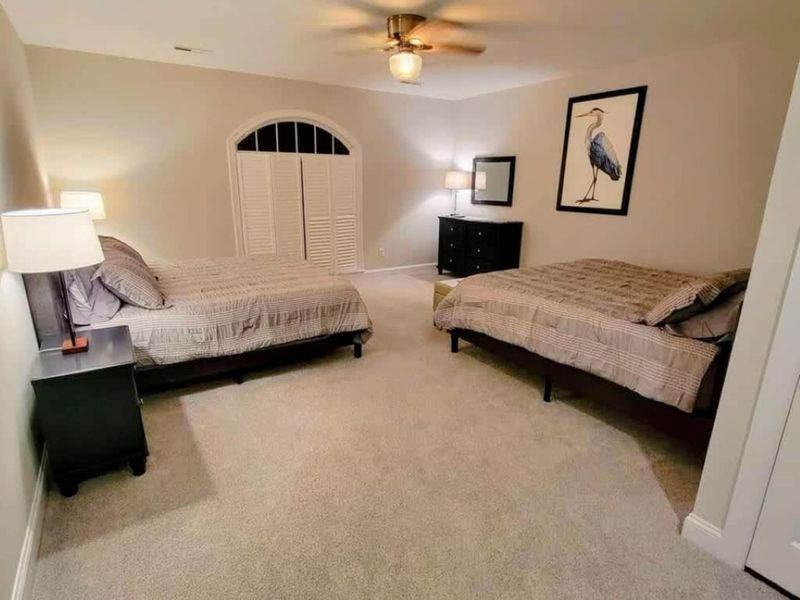 Bedroom - Two full beds with neutral striped bedding, a blue heron print, arched louvered closet, and ceiling fan.