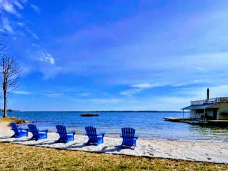 Lakeside serenity: Unwind in colorful Adirondack chairs on your private sandy beach, taking in wide-open views of beautiful Lake Anna under a bright blue sky.
