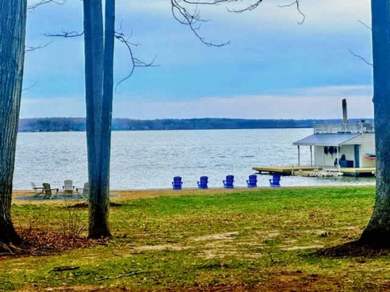 Lakefront retreat: Framed by tall trees, this peaceful view reveals a private beach, inviting chairs, and a charming dock—your perfect escape on the shores of Lake Anna.