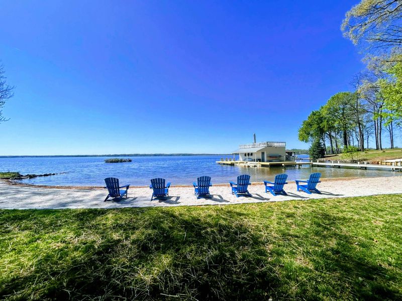 Lakefront comfort: A row of bright Adirondack chairs on your private sandy beach offers the perfect spot to enjoy panoramic Lake Anna views and peaceful shoreline breezes.