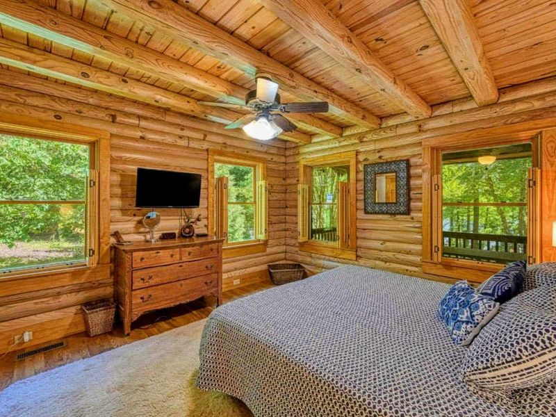 Unwind in this charming log cabin bedroom, surrounded by serene nature views from every window for a truly relaxing escape.