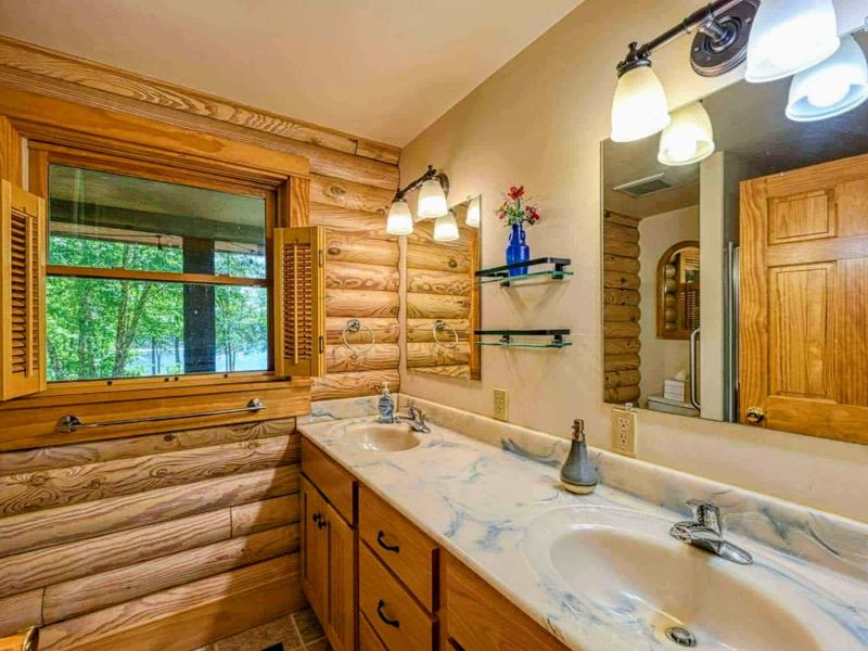 Enjoy the rustic charm of this bathroom with its double sinks, log cabin accents, and a view that brings the outdoors in.