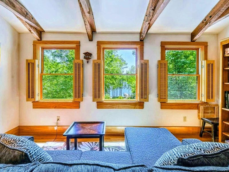 Relax in this cozy living space with stunning views of the lake framed by rustic wooden beams and natural light flooding through the windows.