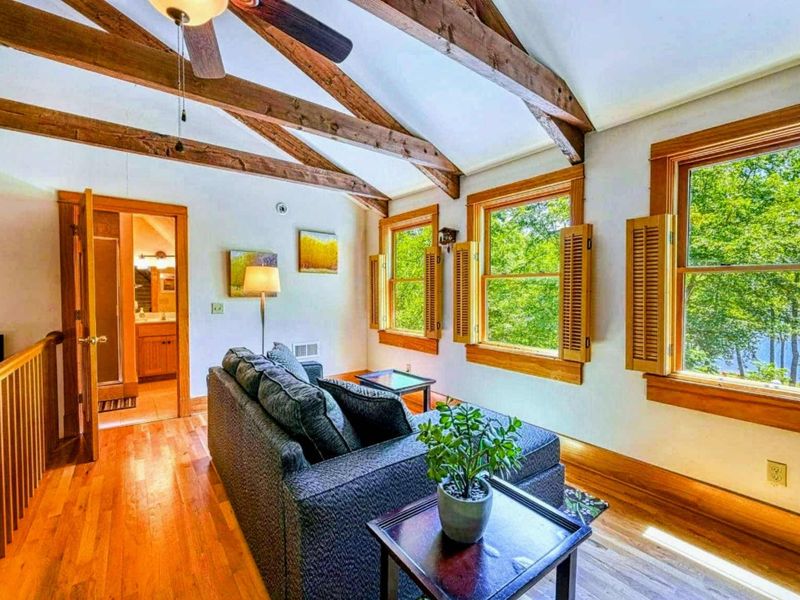 Unwind in this bright and airy living area, where rustic beams meet serene lake views, offering the perfect setting for relaxation.