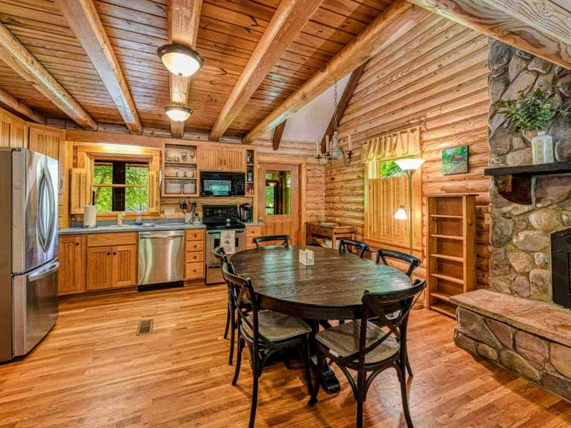 Step into this inviting log cabin kitchen, complete with modern amenities and a cozy dining area by the fireplace, perfect for gathering and creating memories.