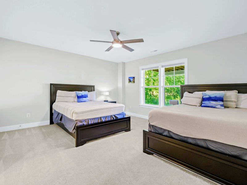 Suite 4 - Two queen beds with dark wood frames, ceiling fan, and a bright window letting in soft natural light all day.