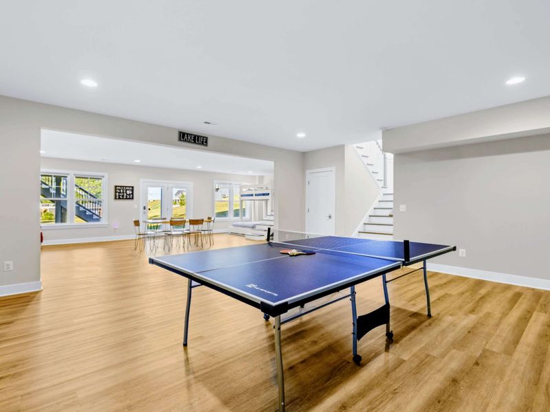 Game Room - View toward the patio doors with a six-seat table, a red velvet armchair, and the bunk room around the corner.