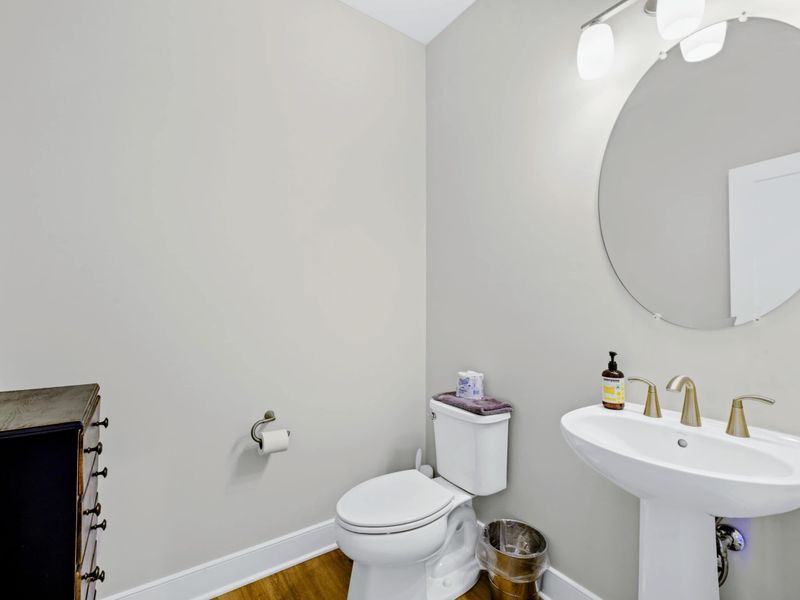 Half Bath - Main-level powder room with pedestal sink, round mirror, and modern lighting for quick guest convenience.
