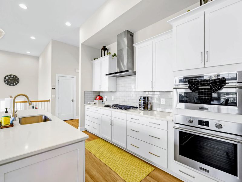 Kitchen - Past the prep sink toward the cooktop and double ovens, with the great room and lake light beyond.