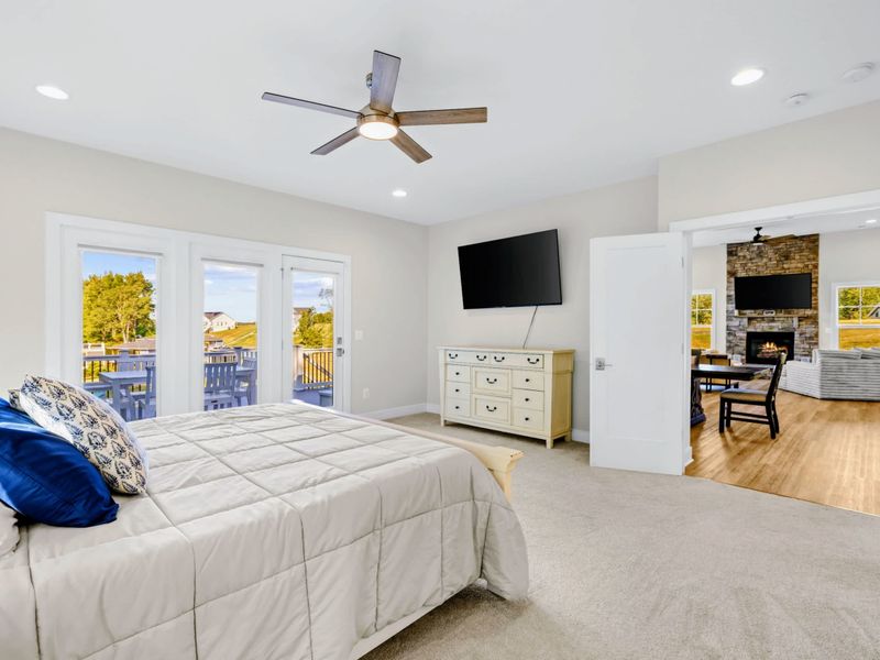 Primary Suite - King bed with mounted TV and dresser, French doors framing the lake view from the private deck.
