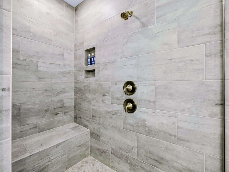 Primary Bath - The walk-in shower interior with built-in bench, niche, and both rainfall and wall-mounted shower heads.