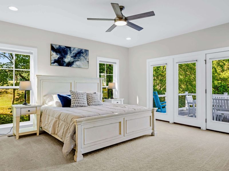 Primary Suite - King bed flanked by twin nightstands, with French doors opening to the back deck and a private morning out.