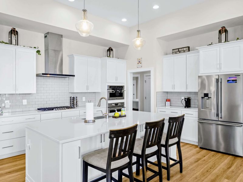 Kitchen - Symmetrical view of the island bar with three stools, gas cooktop, double ovens, and the big French-door fridge.