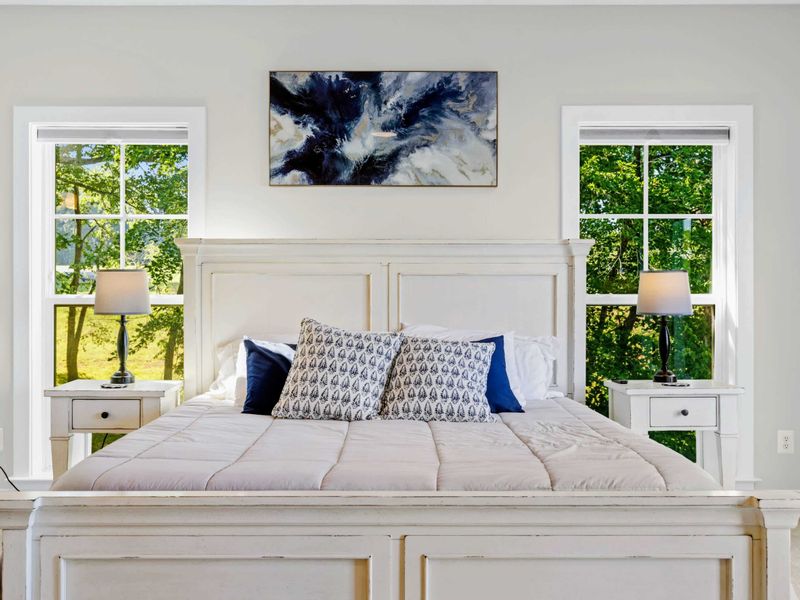 Primary Suite - King bed framed by tall windows over the treetops, with elegant accent artwork above the headboard.