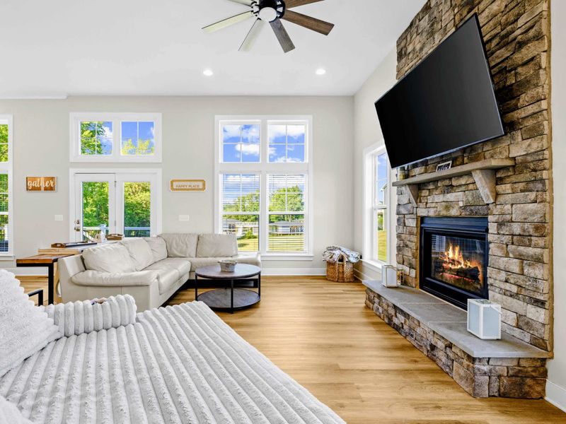 Great Room - Wide view of the lounge with the fireplace lit, soaring windows over the yard, and the dining table just beyond.