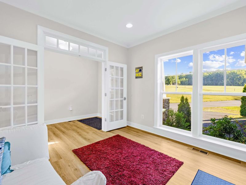 Office - Sun-filled corner with French doors, a wall of windows over the yard, and the great room visible beyond.