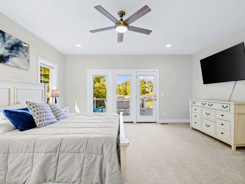 Primary Suite - King bed with mounted TV and dresser, French doors leading to the back deck and the treetops beyond.