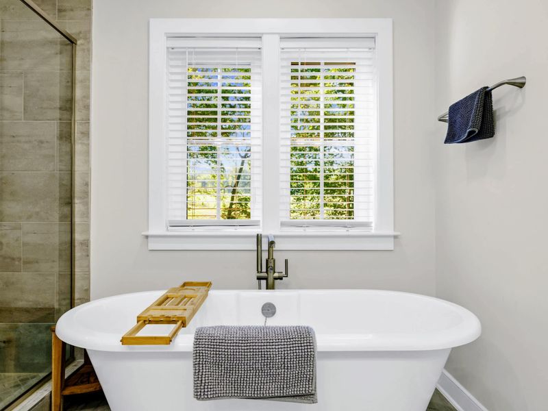 Primary Bath - Freestanding soaking tub with a wooden bath caddy and bright window light overlooking the trees.